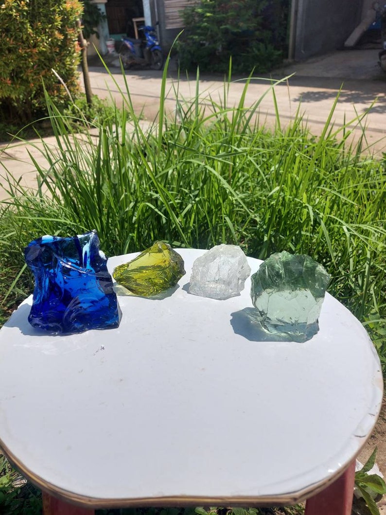 Puede incluir: Cuatro piedras de vidrio de diferentes colores: azul, verde, amarillo y transparente. Las piedras est&aacute;n sobre una mesa blanca.