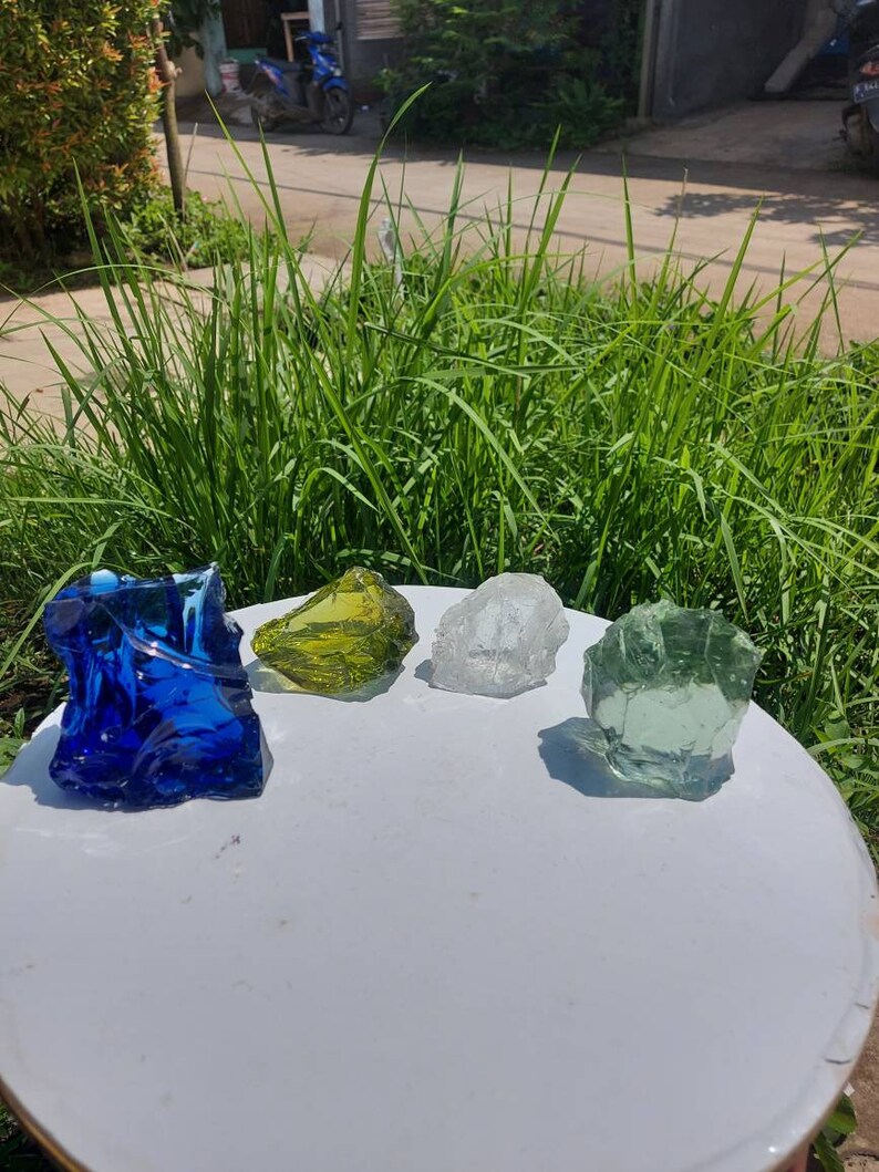 Puede incluir: Cuatro rocas de vidrio en diferentes colores: azul, verde, amarillo y transparente. Las rocas est&aacute;n sobre una superficie blanca.