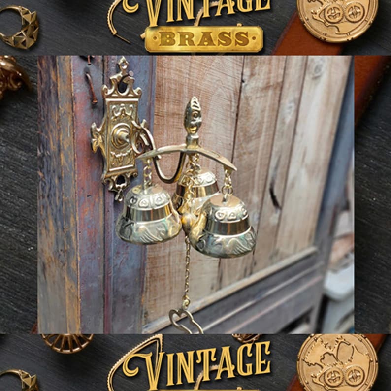 May include: A vintage brass door chime with three bells hanging from a decorative bracket. The chime is attached to a wooden door with a gold-coloured finish. The chime has a chain that hangs down from the bottom bell.
