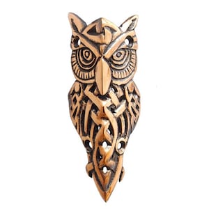 May include: A detailed, copper-colored owl pendant with intricate Celtic knotwork designs. The owl's eyes are large and round, and its beak is pointed. The pendant is a unique and eye-catching piece of jewelry.