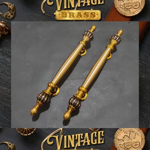 May include: Two gold door handles with black accents and ornate details. The handles are made of brass and have a vintage style.