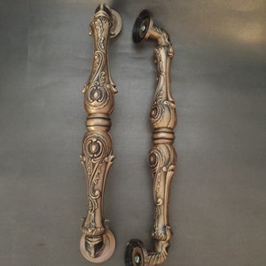 Pode incluir: Um par de ma&ccedil;anetas de porta douradas adornadas com intrincados desenhos florais. As ma&ccedil;anetas s&atilde;o feitas de metal e t&ecirc;m um acabamento polido.