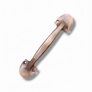 May include: A metallic door handle with a warm, brushed bronze finish. The handle features a central bar with faceted edges and two rounded mounting plates at each end, each containing two pre-drilled screw holes for secure installation.