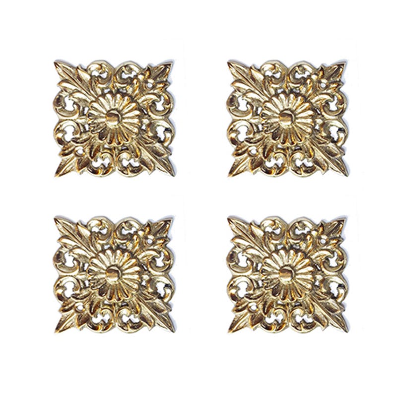 May include: Four gold-toned metal decorative embellishments with a floral design. Each embellishment is square-shaped with intricate details and a raised center.