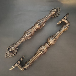Pode incluir: Duas ma&ccedil;anetas de porta ornamentadas de estilo antigo com acabamento dourado e desenhos florais intrincados. As ma&ccedil;anetas s&atilde;o de metal e t&ecirc;m uma forma longa e fina.