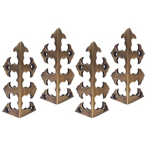 May include: Set of four antique brass corner brackets with a decorative, intricate design. Each bracket features a pointed, leaf-like shape with multiple cutouts.