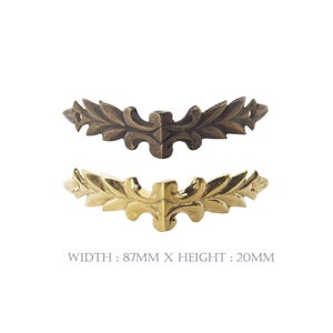 May include: Two decorative metal corner brackets. One is bronze-colored, the other is gold-colored. Each has a leaf and scroll design. The text at the bottom reads: WIDTH: 87mm X HEIGHT: 20mm.