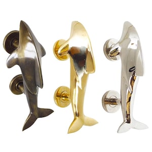 Könnte beinhalten: Drei Delfin-Türklopfer in verschiedenen Ausführungen: Antikmessing, poliertes Messing und poliertes Nickel.