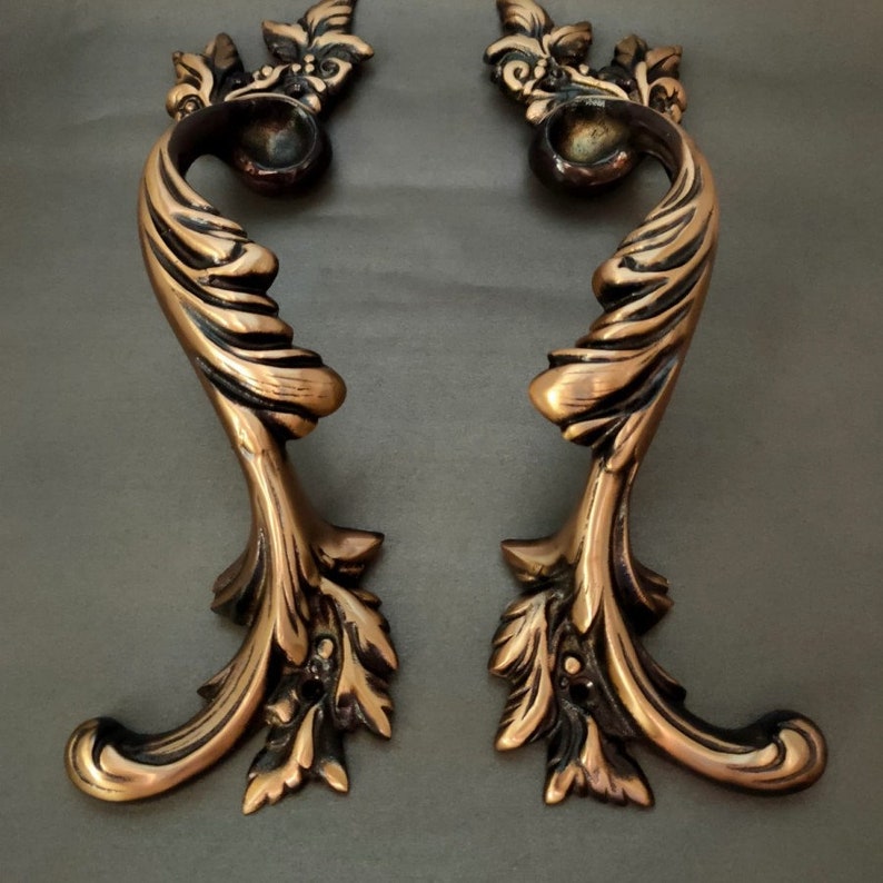 May include: A pair of ornate, antique-style door handles with a bronze finish. The handles are intricately designed with swirling patterns and leaf motifs.