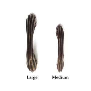 Pode incluir: Duas puxadores de armário em tom bronze, um grande e um médio, contra um fundo branco. Os puxadores têm um design canelado e são rotulados como "Large" e "Medium" na base. Estes puxadores decorativos são adequados para móveis ou armários.
