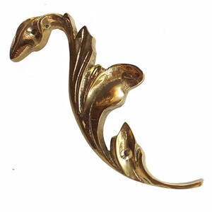 May include: A gold-colored metal decorative leaf design with a stylized, flowing shape. The leaf is made of brass and has a smooth, polished finish.