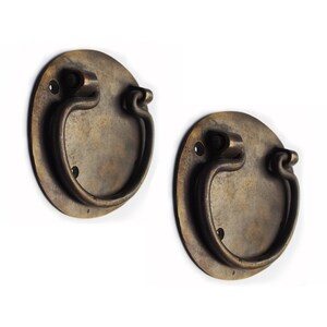 May include: Two antique brass door pulls with a rounded, oval shape and a decorative ring handle. The pulls have a distressed, aged finish.