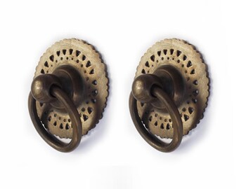May include: Two antique brass cabinet knobs with a decorative, intricate, circular design. The knobs have a ring pull and are perfect for adding a vintage touch to furniture.