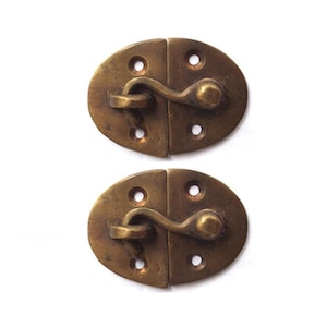 Op de afbeelding: Twee antieke messing ovale kastdeurgrepen met een haak en een ronde knop.