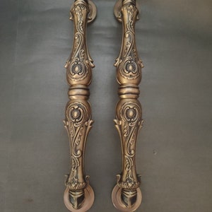 Pode incluir: Um par de ma&ccedil;anetas de porta douradas ornamentadas com intrincados desenhos florais. As ma&ccedil;anetas s&atilde;o feitas de metal e t&ecirc;m um acabamento polido.