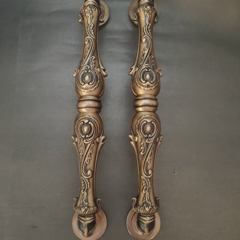 Pode incluir: Um par de ma&ccedil;anetas de porta douradas ornamentadas com intrincados desenhos florais. As ma&ccedil;anetas s&atilde;o feitas de metal e t&ecirc;m um acabamento polido.