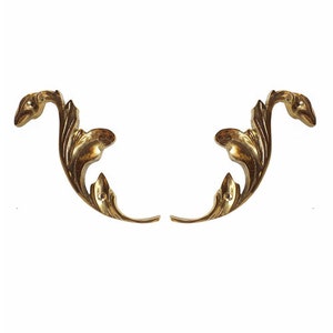 May include: Two gold-colored metal decorative accents with a leaf design. The accents are symmetrical and have a curved shape.
