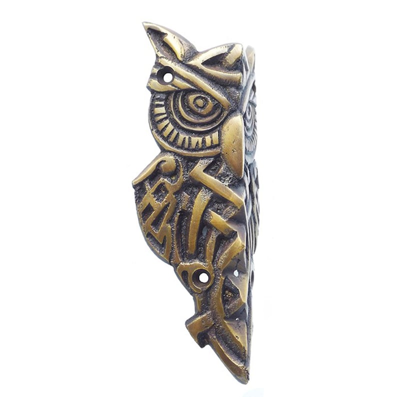 May include: A brass owl wall hook with intricate geometric designs. The owl's eyes are detailed and the hook is shaped like the owl's body.