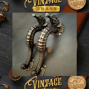 Könnte beinhalten: Zwei verzierte Messing-Türgriffe in Form von Seepferdchen. Die Griffe sind mit strukturierten Schuppen verziert und haben eine Vintage-Ästhetik.