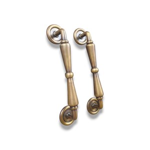 May include: A pair of antique brass cabinet pulls with a classic design. Each pull has a curved handle and circular backplates. The hardware has a warm, aged finish, suggesting a vintage or traditional style.