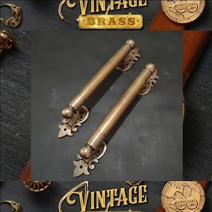 Peut inclure: Deux poignées de porte en laiton vintage avec des motifs ornés. Les poignées sont longues et fines avec une extrémité arrondie. Les poignées sont en laiton massif et ont une finition polie.