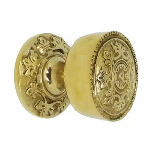 May include: A pair of antique brass door knobs. One knob is round with a floral design, and the other is a circular plate with a floral design. The door knobs are a warm gold colour.