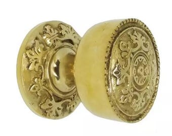 Op de afbeelding: Een paar antieke messing deurknoppen. De ene knop is rond met een bloemmotief en de andere is een cirkelvormige plaat met een bloemmotief. De deurknoppen hebben een warme goudkleur.