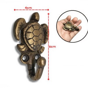 May include: A bronze-coloured turtle-shaped wall hook, measuring approximately 4 cm wide and 6 cm tall. The hook features a detailed turtle design with a hook extending from the bottom. A smaller version of the hook is shown in a hand.