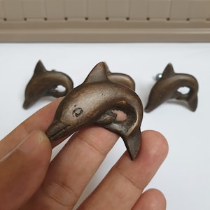 May include: Three bronze dolphin door knobs with a detailed design. The dolphins are facing to the right and have a smooth, polished finish.