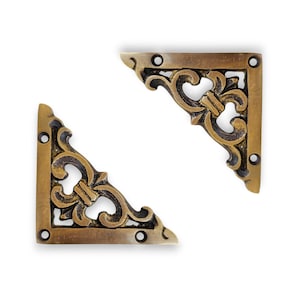 May include: Two antique brass corner brackets with ornate, symmetrical scrollwork and three screw holes each. The brackets are a warm, aged gold color, and are set against a white background.