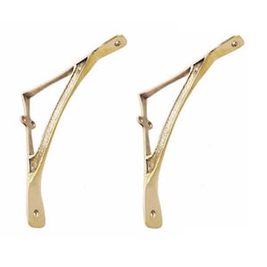 May include: Two gold metal shelf brackets with a decorative design. The brackets are shaped like a triangle with a curved top.