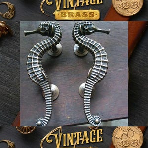 May include: A pair of vintage brass door handles shaped like seahorses. The handles are detailed with a textured finish and have a dark patina.