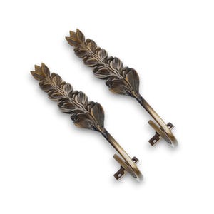 Puede incluir: Dos recogedores de cortinas de color bronce. Cada recogedor presenta un diseño detallado de hojas y un gancho curvo para sujetar las cortinas. Los recogedores están hechos de metal y están diseñados para montarse en la pared.