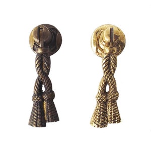 May include: Two brass cabinet knobs with a rope design. The knobs are in different finishes, one is a darker brass and the other is a lighter brass.