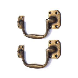Può includere: Due maniglie per armadi in ottone antico con una piastra posteriore quadrata e una maniglia curva. Le maniglie sono in ottone massiccio e hanno una finitura lucida.