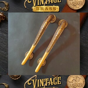 May include: Two ornate brass door handles with intricate designs. The handles are long and slender with a curved shape. They have a vintage look and feel.