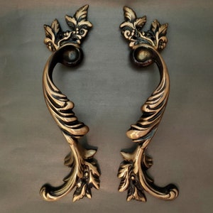 May include: Two ornate, gold-toned cabinet pulls with a leaf and scroll design. The pulls have a decorative, antique look.