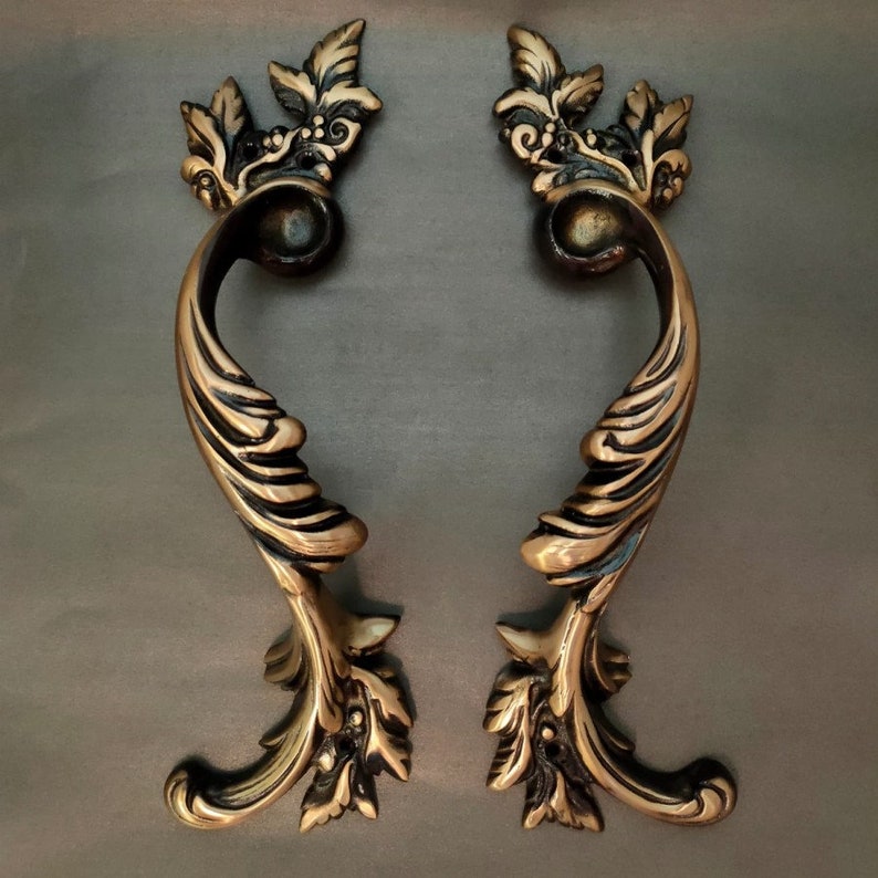 May include: Two ornate, gold-toned cabinet pulls with a leaf and scroll design. The pulls have a decorative, antique look.