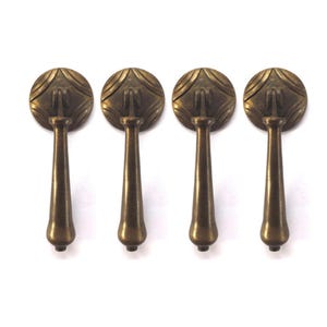 May include: Four antique brass cabinet pulls with a decorative design. Each pull has a round top with a raised design and a long, slender stem.