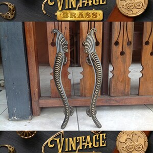 May include: Two ornate, vintage brass door handles with a decorative, swirling design. The handles are mounted on a wooden door.