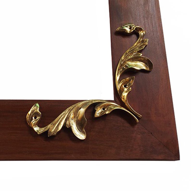 May include: A close-up of a wooden picture frame with gold leaf corner accents. The frame is a rich mahogany color and the corner accents are intricate and detailed.