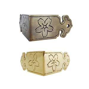 May include: Two decorative corner brackets. One is bronze-toned, the other gold-toned. Each features a floral design and ornate edges. These metal brackets are designed to protect and embellish the corners of furniture or boxes.