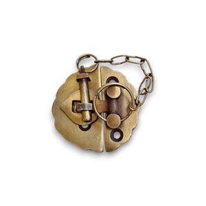 May include: A vintage brass clasp with a decorative, scalloped edge. The clasp features two hinged halves, a central locking mechanism, and a small chain. The metal has a warm, antique finish, suggesting age and use.