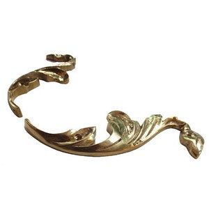 May include: A pair of gold-tone metal decorative corner brackets with a scroll design. The brackets are designed to be used as a decorative element for furniture or other home decor projects.