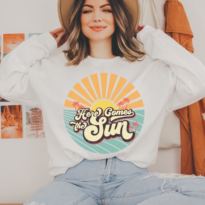 May include: White sweatshirt with a retro sun graphic and the text "Here Comes the Sun".