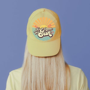 May include: A yellow baseball cap with a retro sun graphic and the text "Here Comes the Sun".