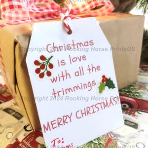 May include: White gift tag with red text that reads "Christmas is love with all the trimmings. Merry Christmas!"  The tag has a red and white gingham ribbon attached to it.  The tag is tied to a brown gift box with a red and white gingham bow.