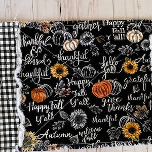 May include: A long, rectangular table runner with a black and white checkered pattern and a central panel featuring pumpkins, sunflowers, and fall-themed script. The runner has a frayed edge and is designed for seasonal home decor.