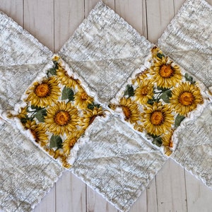May include: A quilted table runner featuring a repeating pattern of sunflowers on a white background. The sunflowers have yellow petals and dark centers. The runner is made of a soft, textured fabric with a ruffled edge.
