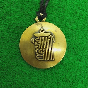May include: A gold-coloured pendant necklace with a black cord. The pendant is round and features a Tibetan prayer wheel symbol.